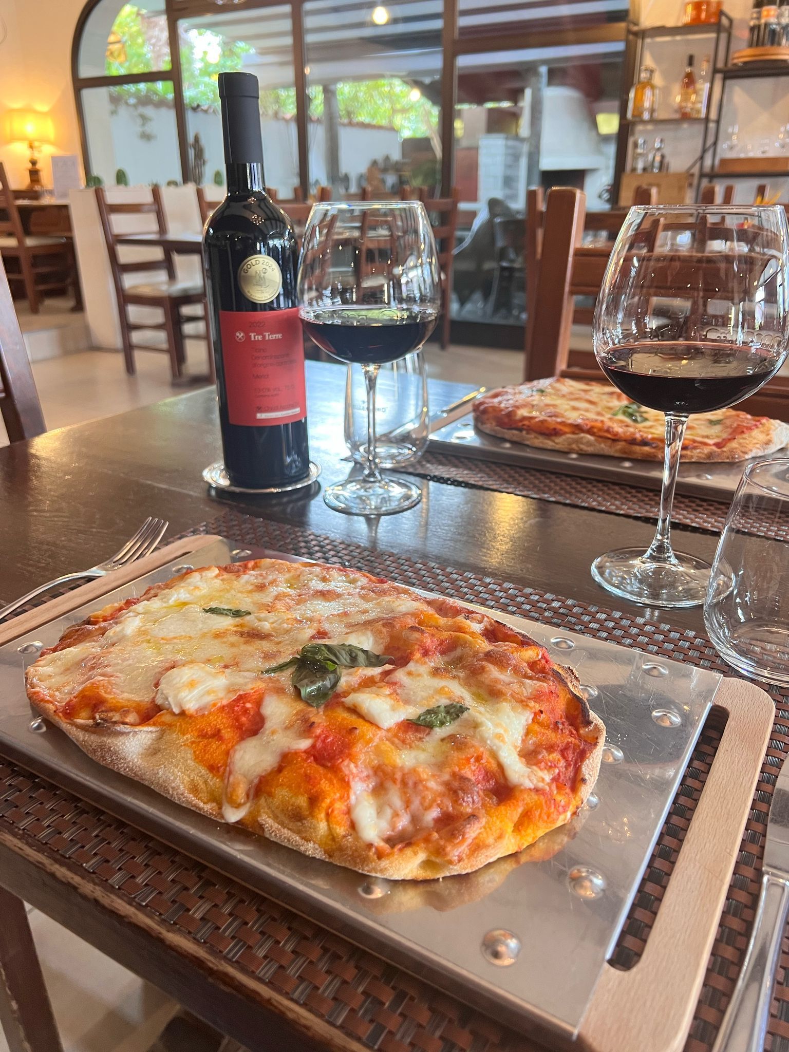 Una pizza è appoggiata su un vassoio di metallo su un tavolo accanto a una bottiglia di vino.