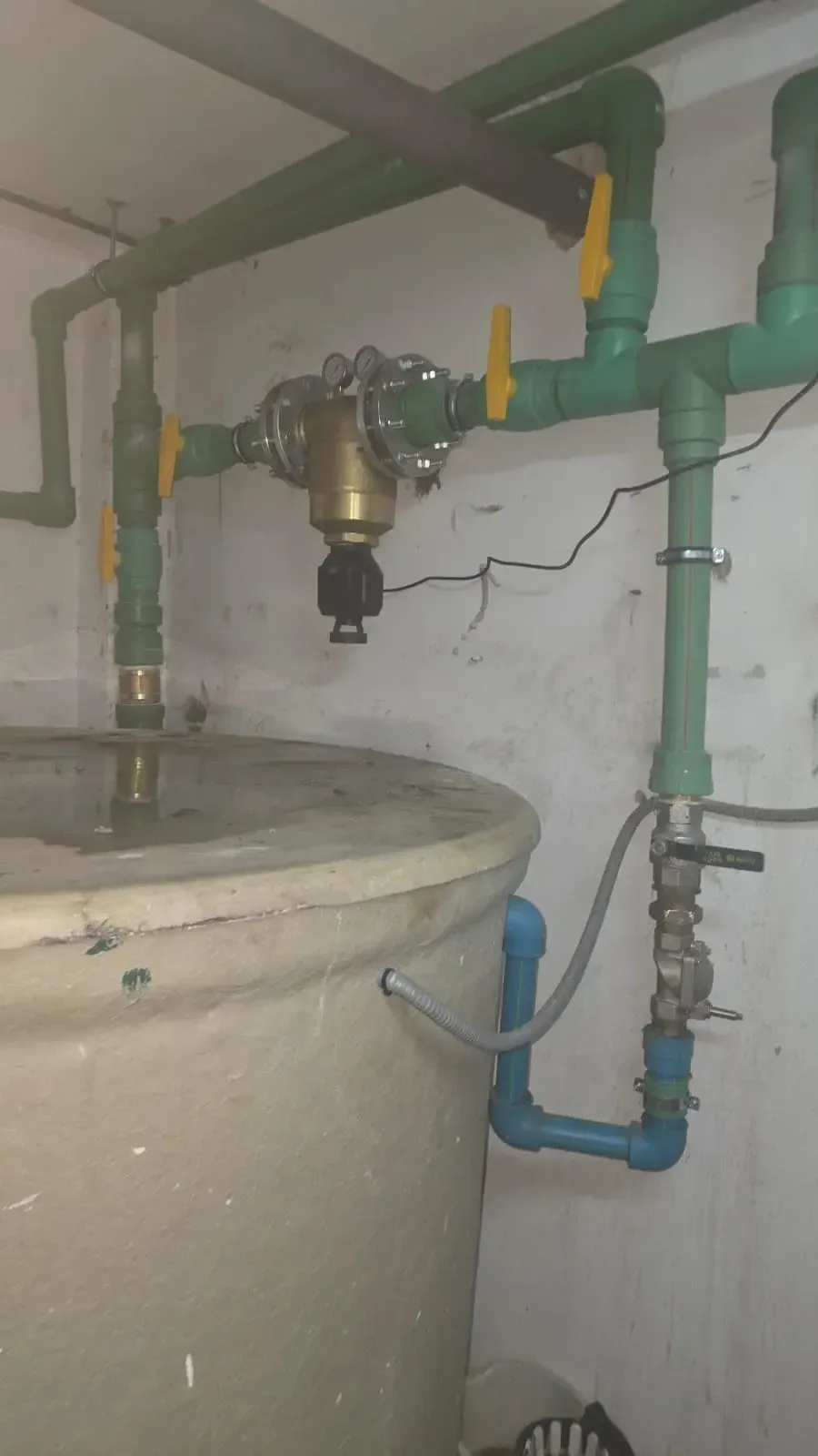 Tuberías y válvulas industriales situadas sobre un gran depósito de color beige, junto a una pared blanca