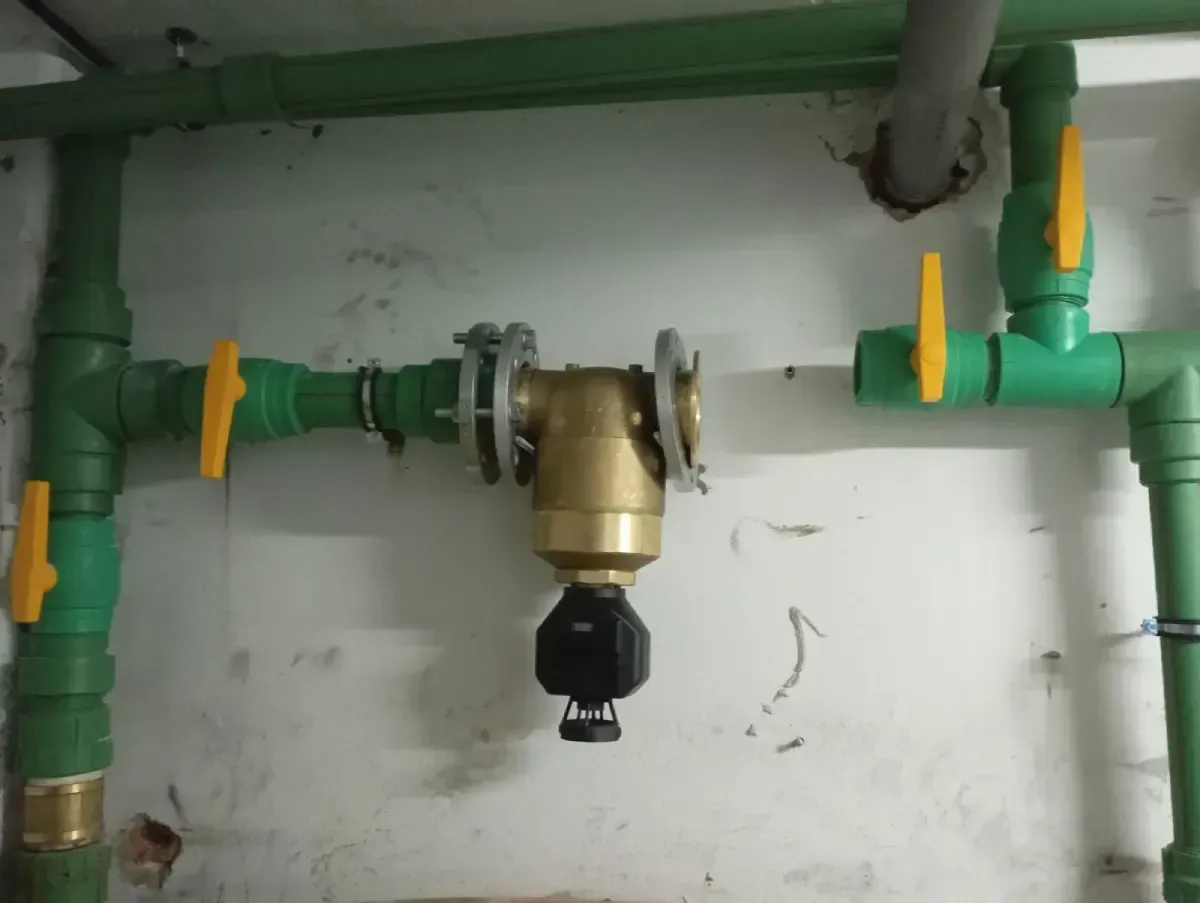 Tuberías verdes y amarillas con una válvula de latón y un conector negro en un área de servicio.