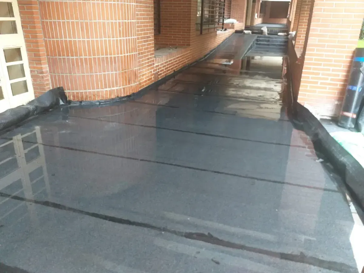 Pasarela cubierta con suelo oscuro y húmedo entre muros de ladrillo y columnas.