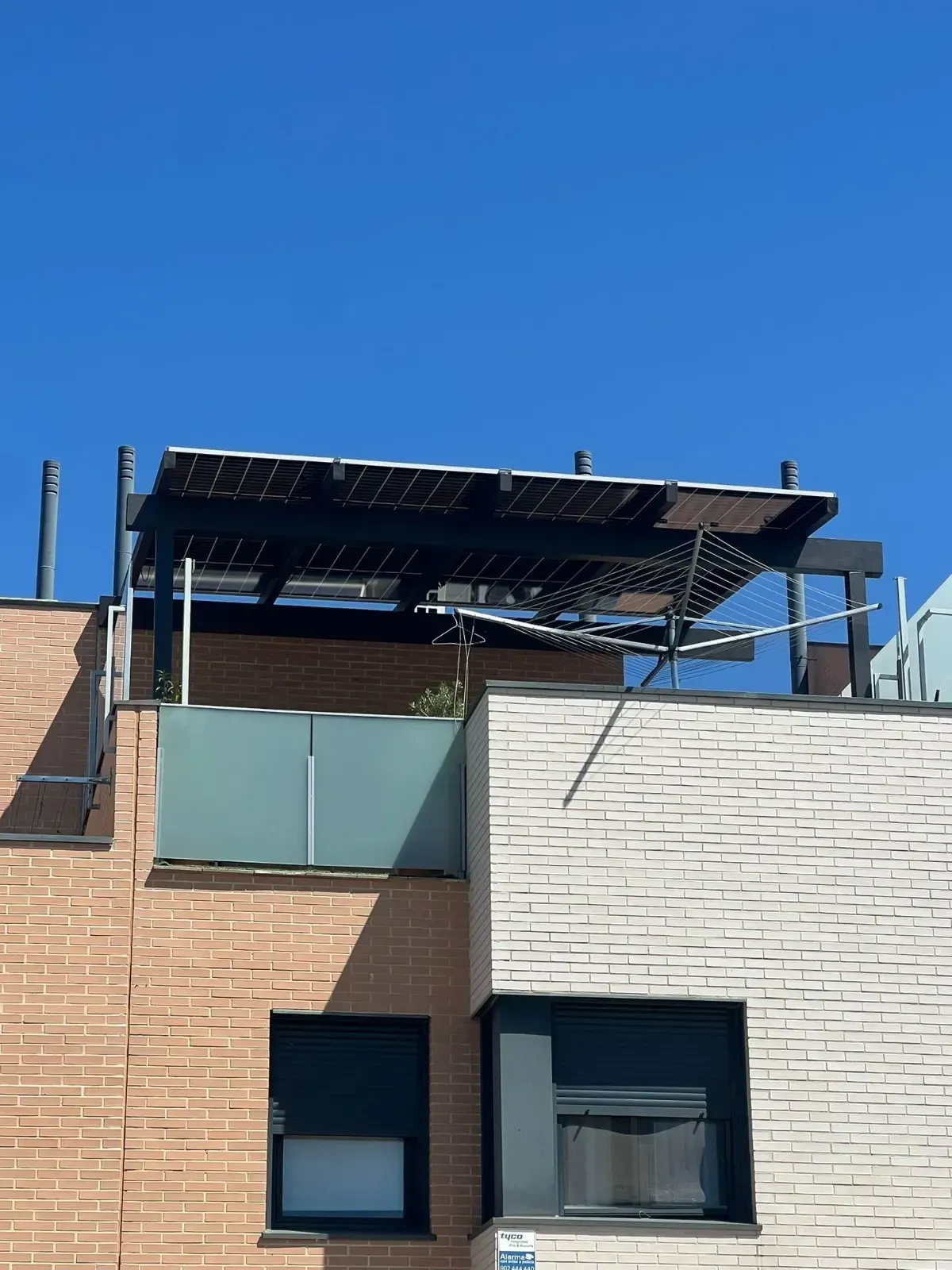 Paneles solares instalados en la azotea de un edificio de apartamentos de ladrillo bajo un cielo azul despejado.