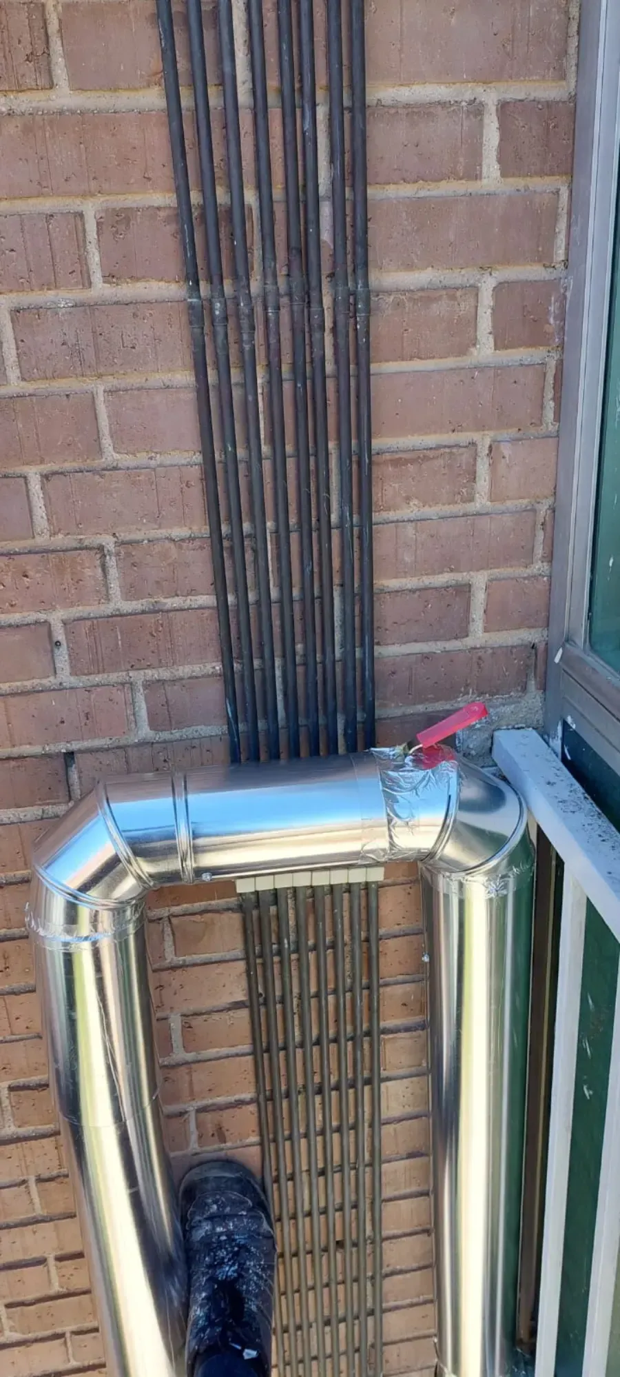 Conducto metálico para cables que recorre una pared de ladrillos junto a una rejilla de ventilación