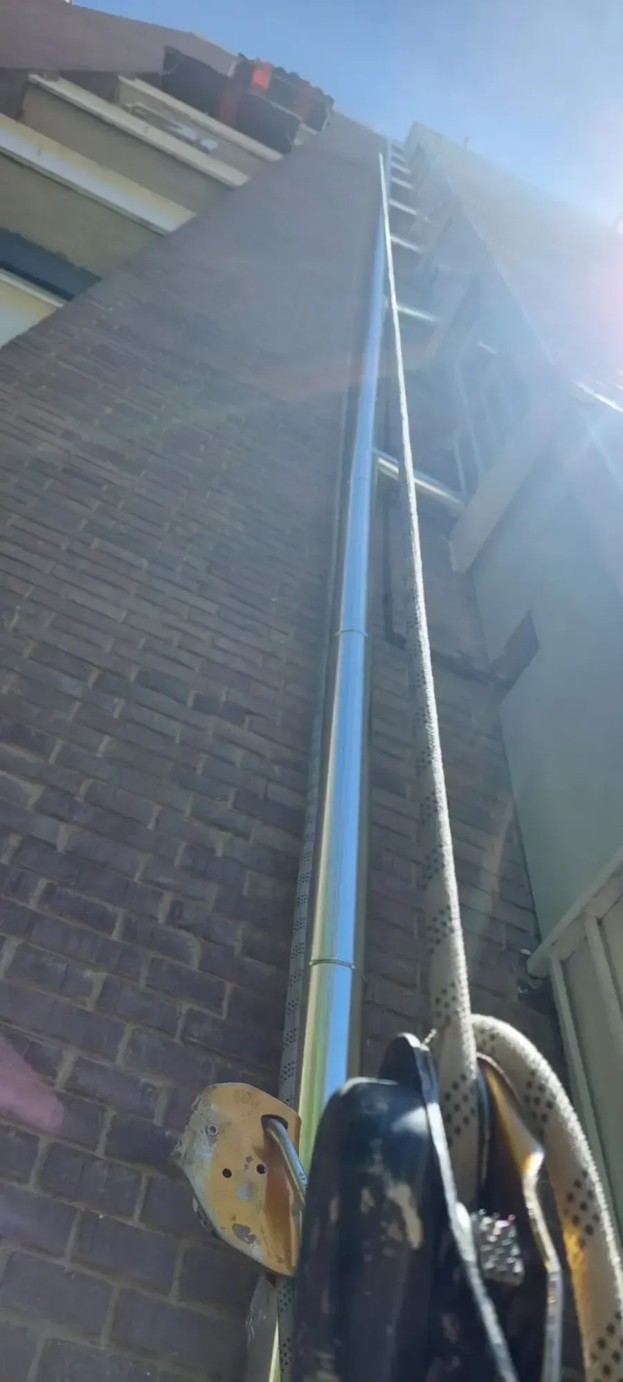 Muro de ladrillo con una larga escalera metálica que se extiende hacia arriba, bajo la brillante luz del sol.