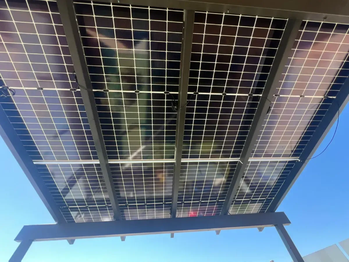 Paneles solares instalados en lo alto, con un cielo azul de fondo, vistos desde abajo.