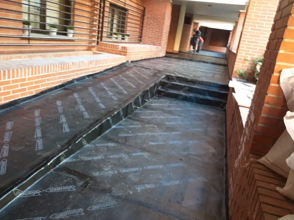 Pasarela cubierta de ladrillo con rampa de acceso inclinada y escalones, que conduce a un pasillo.
