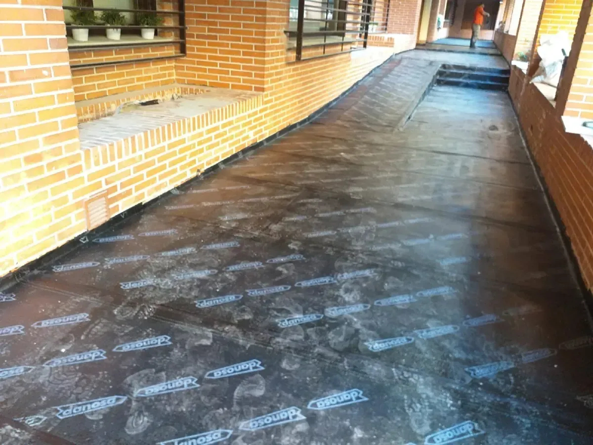 Pasarela de ladrillos cubierta con un suelo oscuro y húmedo junto a un edificio.