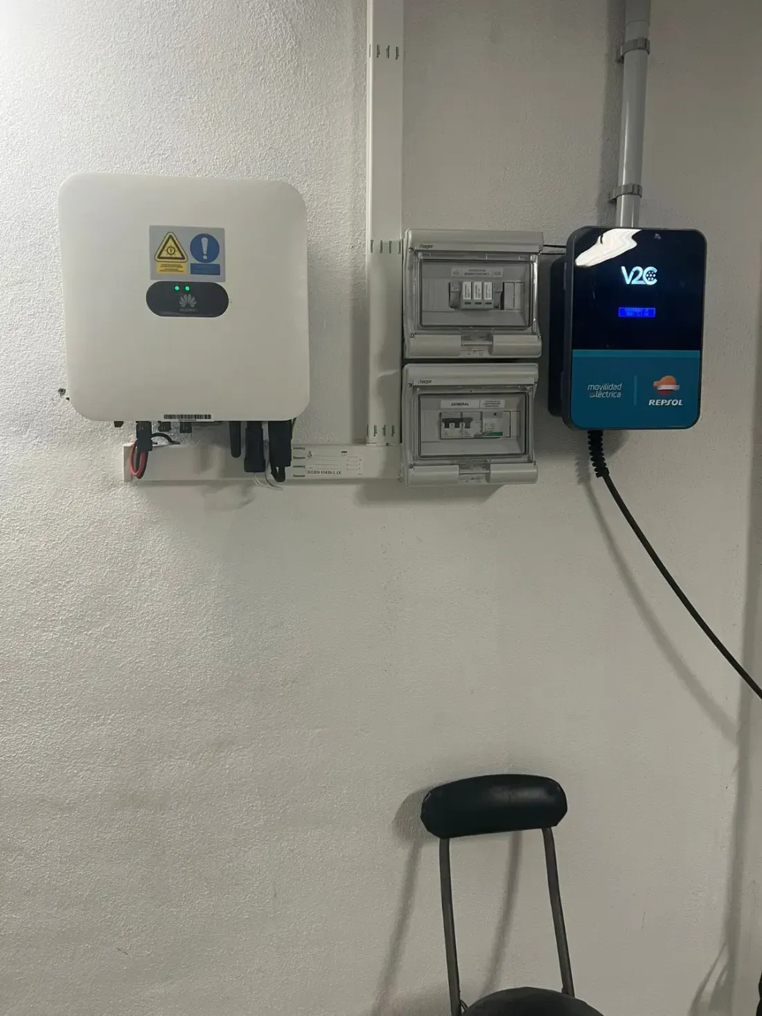 Equipo eléctrico montado en la pared y un inversor digital azul en una pared blanca encima de un taburete.
