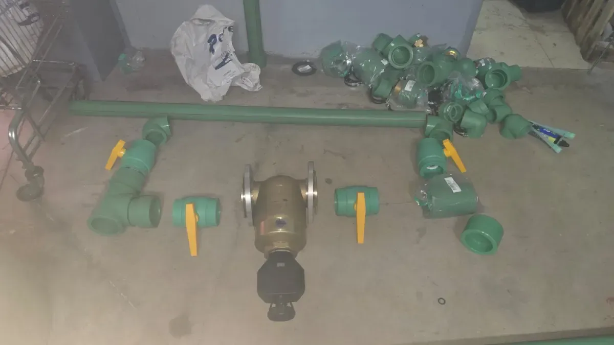 Varias herramientas y piezas de metal verde dispuestas en el suelo, con un taladro en el centro.