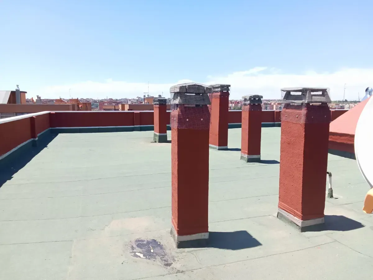 Azotea con chimeneas de ladrillo rojo y superficie verde bajo un cielo azul despejado.