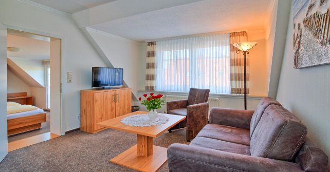 Ein Wohnzimmer mit Couch, Sessel, Tisch und Fernseher.