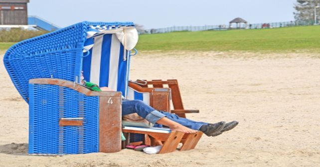 Eine Person liegt in einem blau-weißen Stuhl am Strand