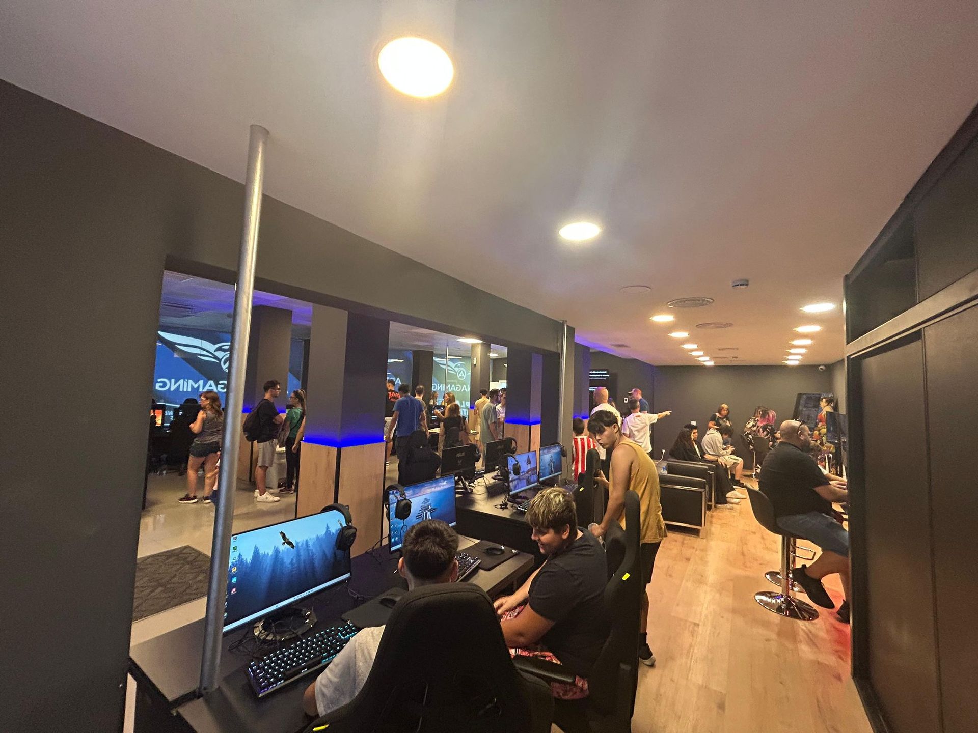 Jugadores en un área de juegos bien iluminada con computadoras, socializando y jugando.