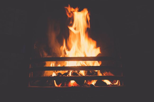 Un feu brûle dans une cheminée derrière des barreaux de métal noir.