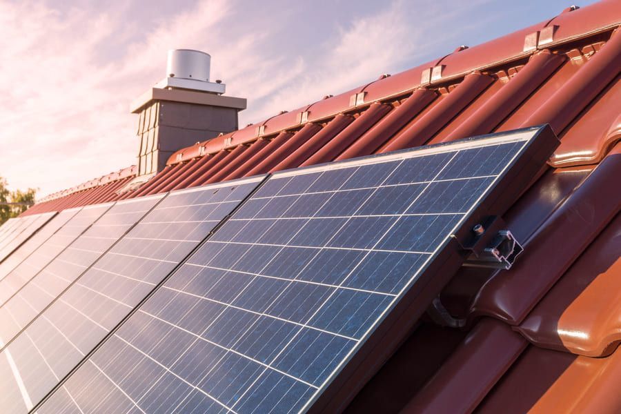Des panneaux solaires installés sur un toit de tuiles rouges sous un ciel rose