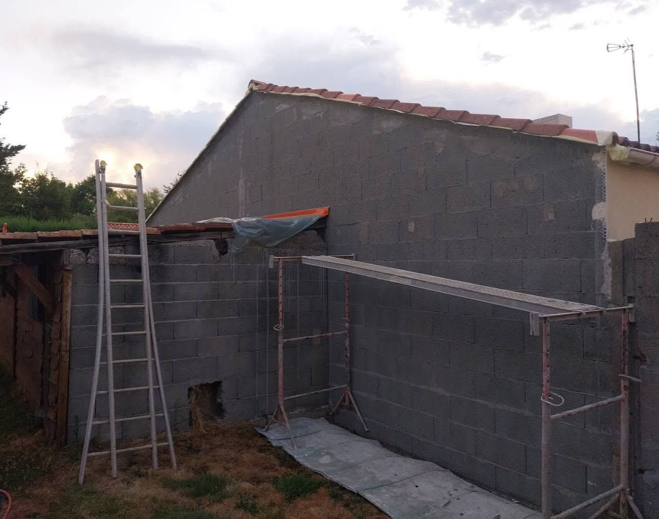 Maison en parpaings partiellement construite, avec échelles et échafaudages