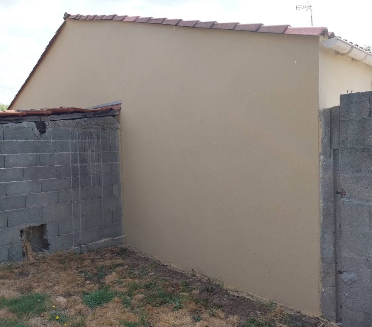 Mur extérieur beige entre des murs en parpaings sous un toit de tuiles