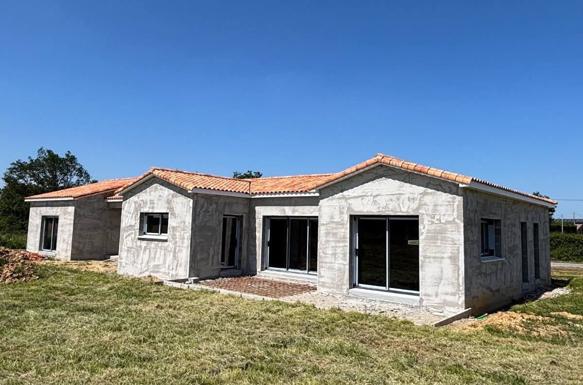 Maison de plain-pied partiellement construite, aux murs gris inachevés et au toit de tuiles rouges