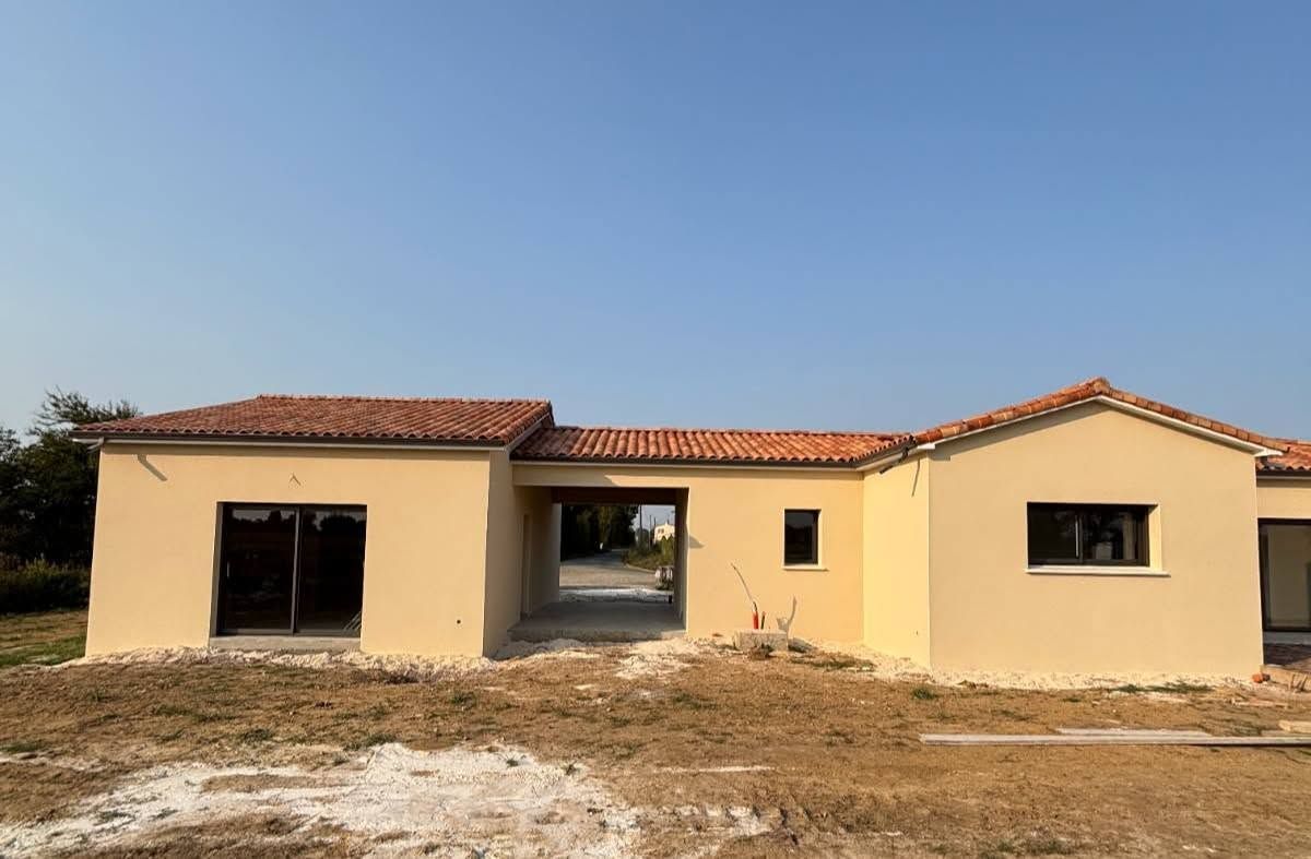 Maison beige de plain-pied au toit de tuiles rouges, sous un ciel bleu azu