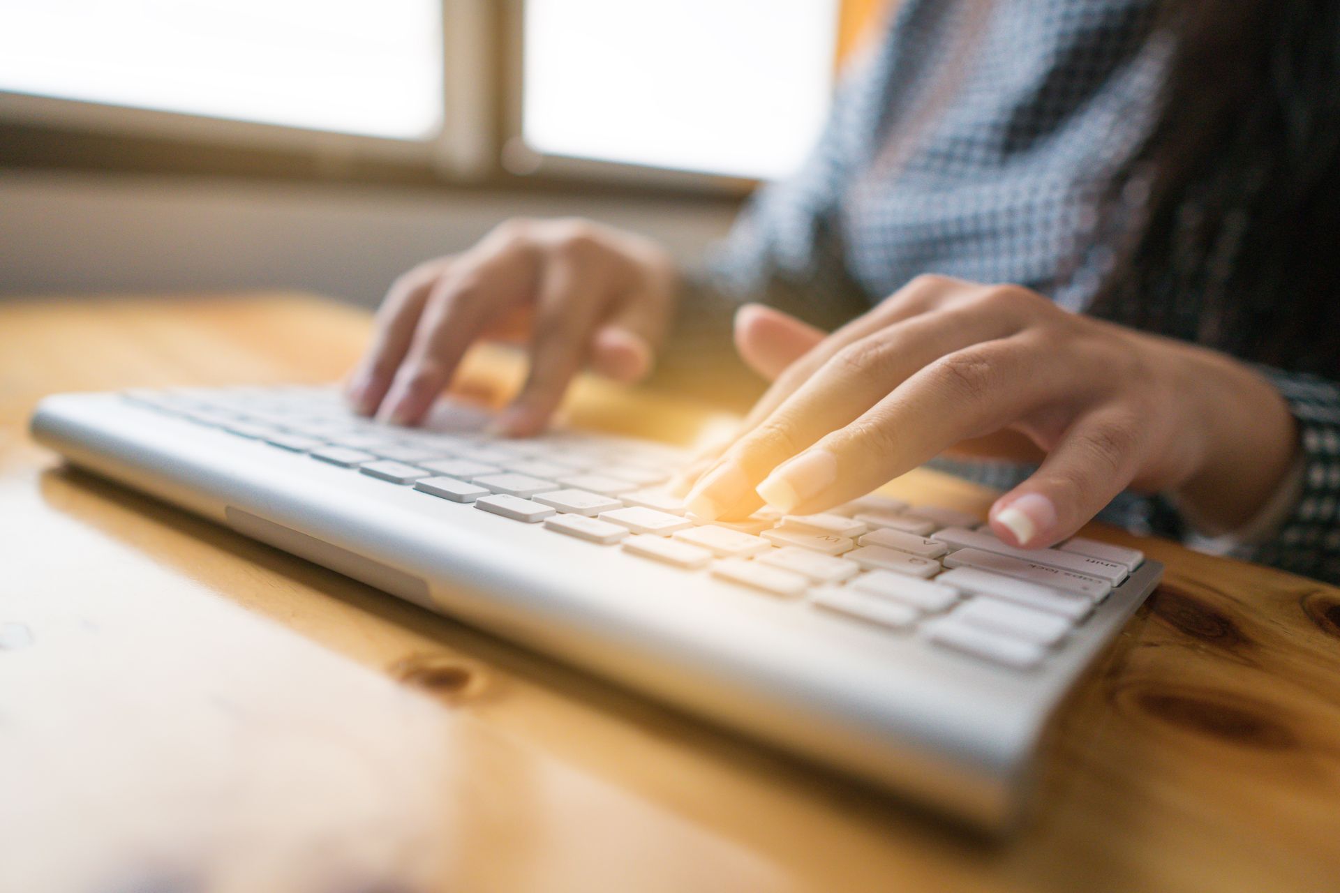 Mains tapant sur un clavier argenté, posé sur un bureau en bois.