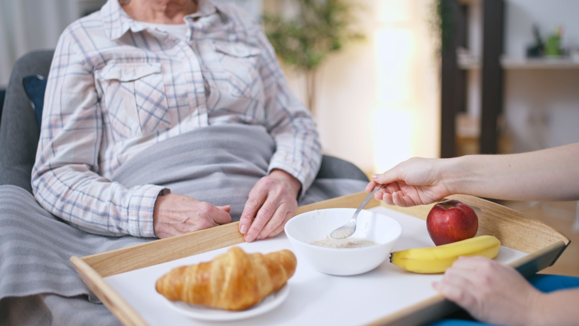 Une personne au lit prend son petit-déjeuner. Un plateau de nourriture est posé devant elle.