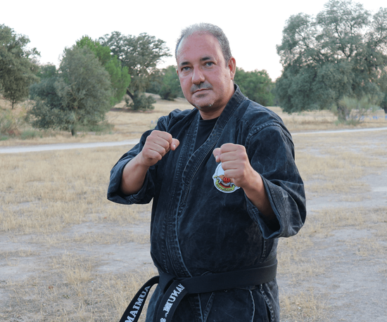 Un hombre con un uniforme de karate negro está parado en un campo.