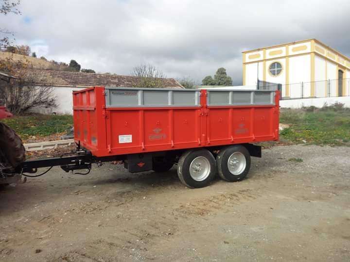 Un remolque rojo está estacionado en un camino de tierra frente a un edificio.