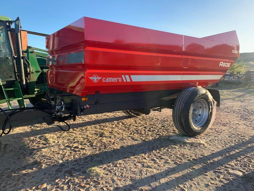 Un remolque rojo está estacionado en la tierra al lado de un tractor.
