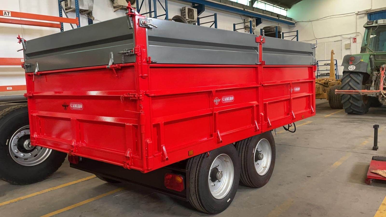 Un remolque rojo está estacionado en un garaje al lado de un tractor.