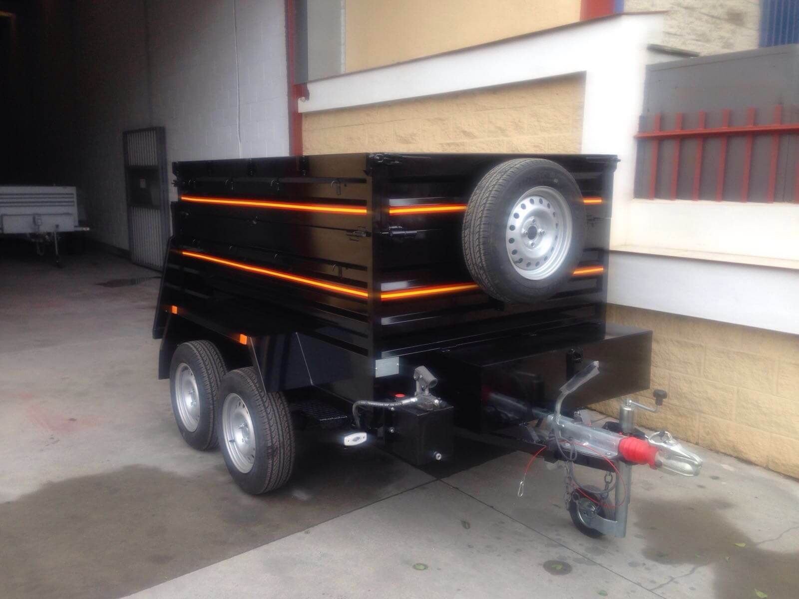 Un remolque negro con una llanta de repuesto en la parte trasera está estacionado frente a un edificio.