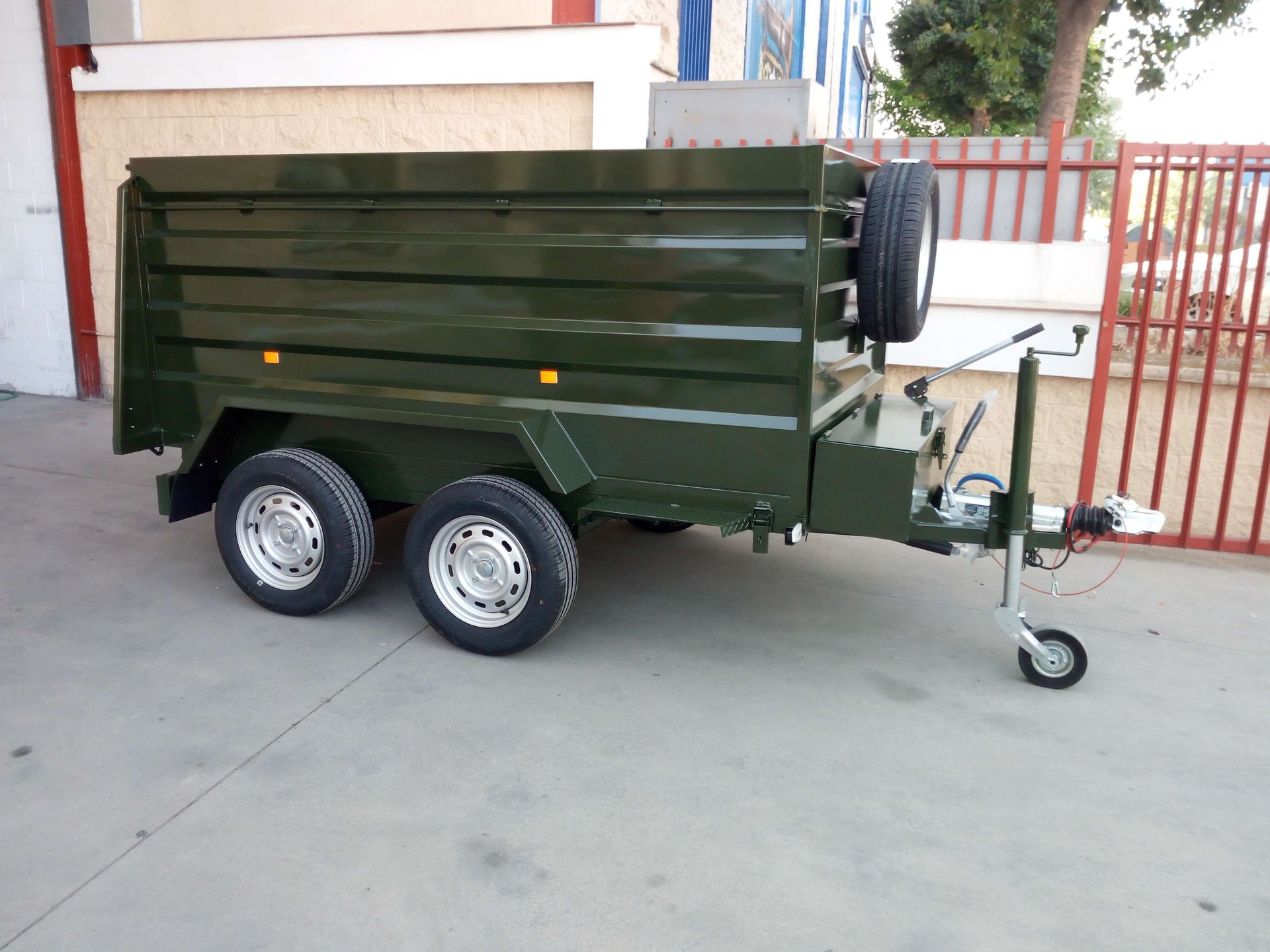 Un remolque verde está estacionado frente a una valla.