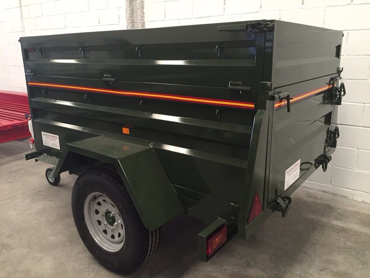 Un remolque verde está estacionado frente a una pared de ladrillos blancos.