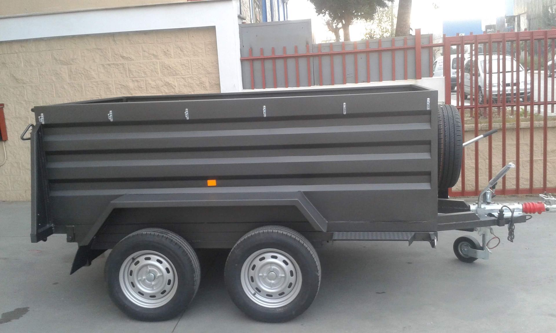 Un remolque negro está estacionado frente a una valla.