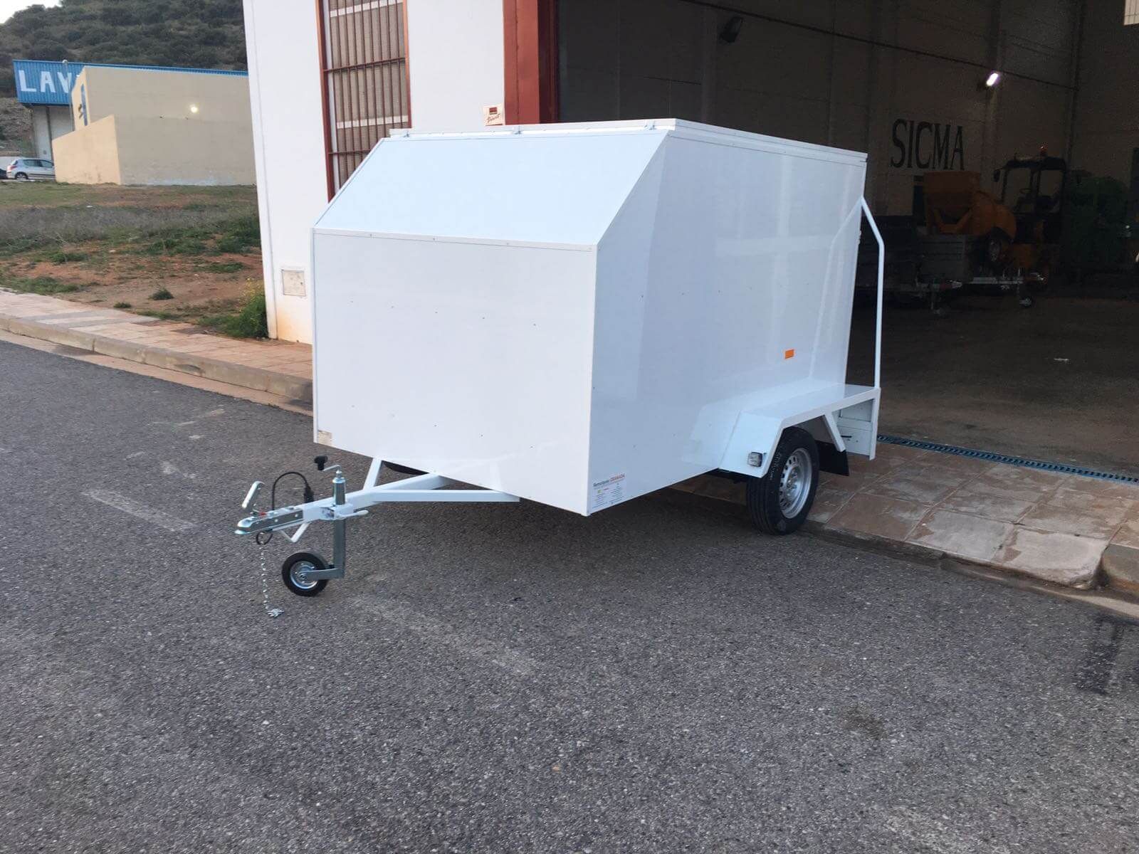 Un remolque blanco está estacionado al costado de la carretera frente a un edificio.