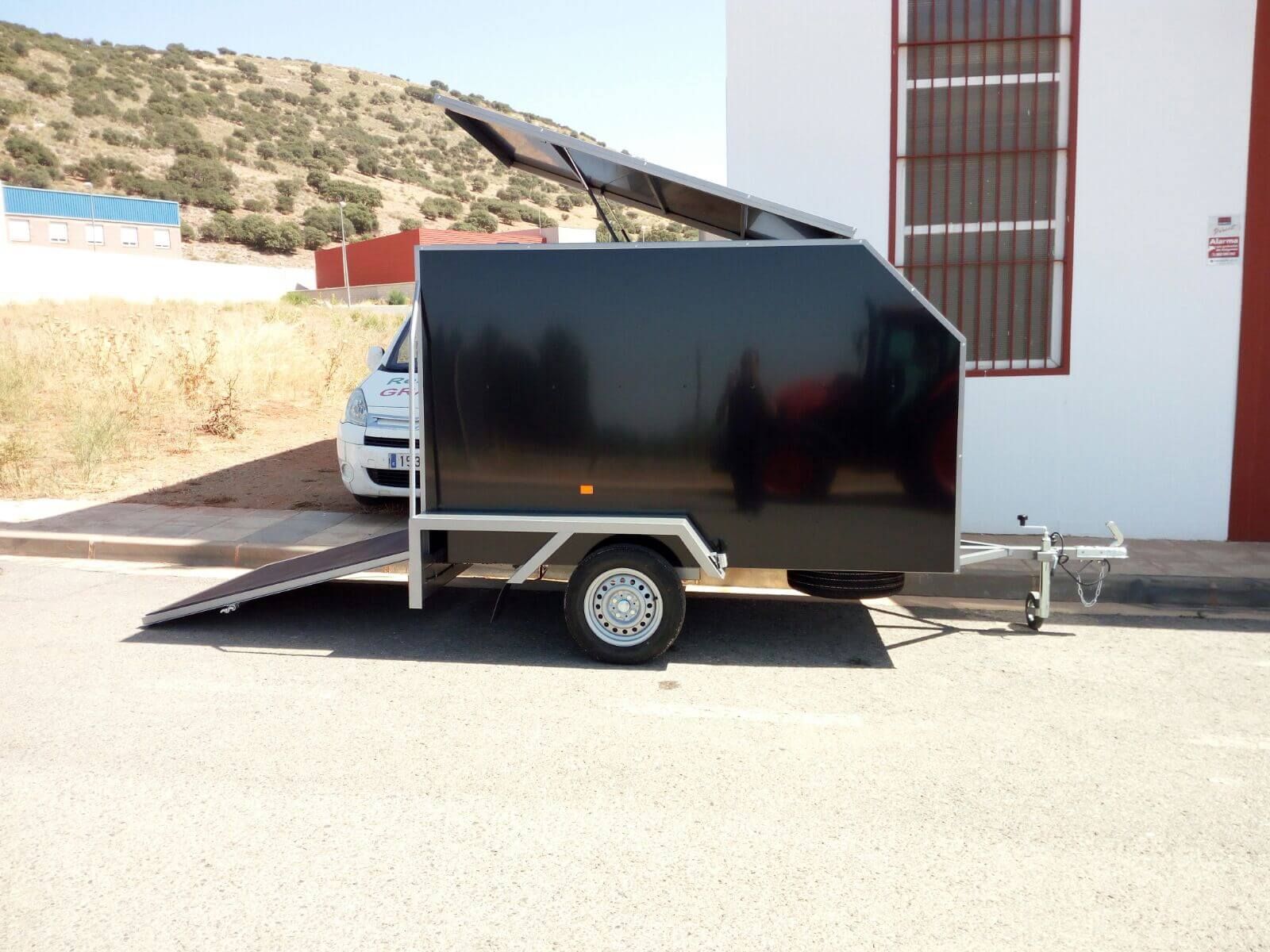 Un remolque negro está estacionado frente a un edificio blanco.