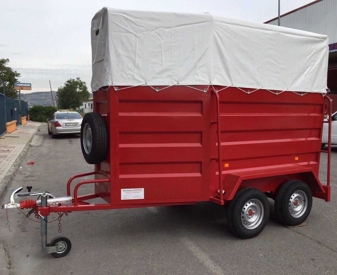 Un remolque rojo con un toldo blanco está estacionado al costado de la carretera.