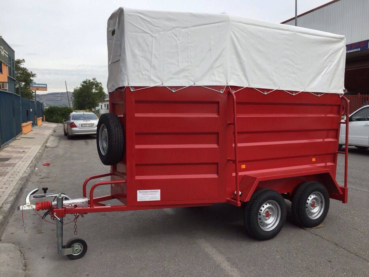 Un remolque rojo con un toldo blanco está estacionado al costado de la carretera.