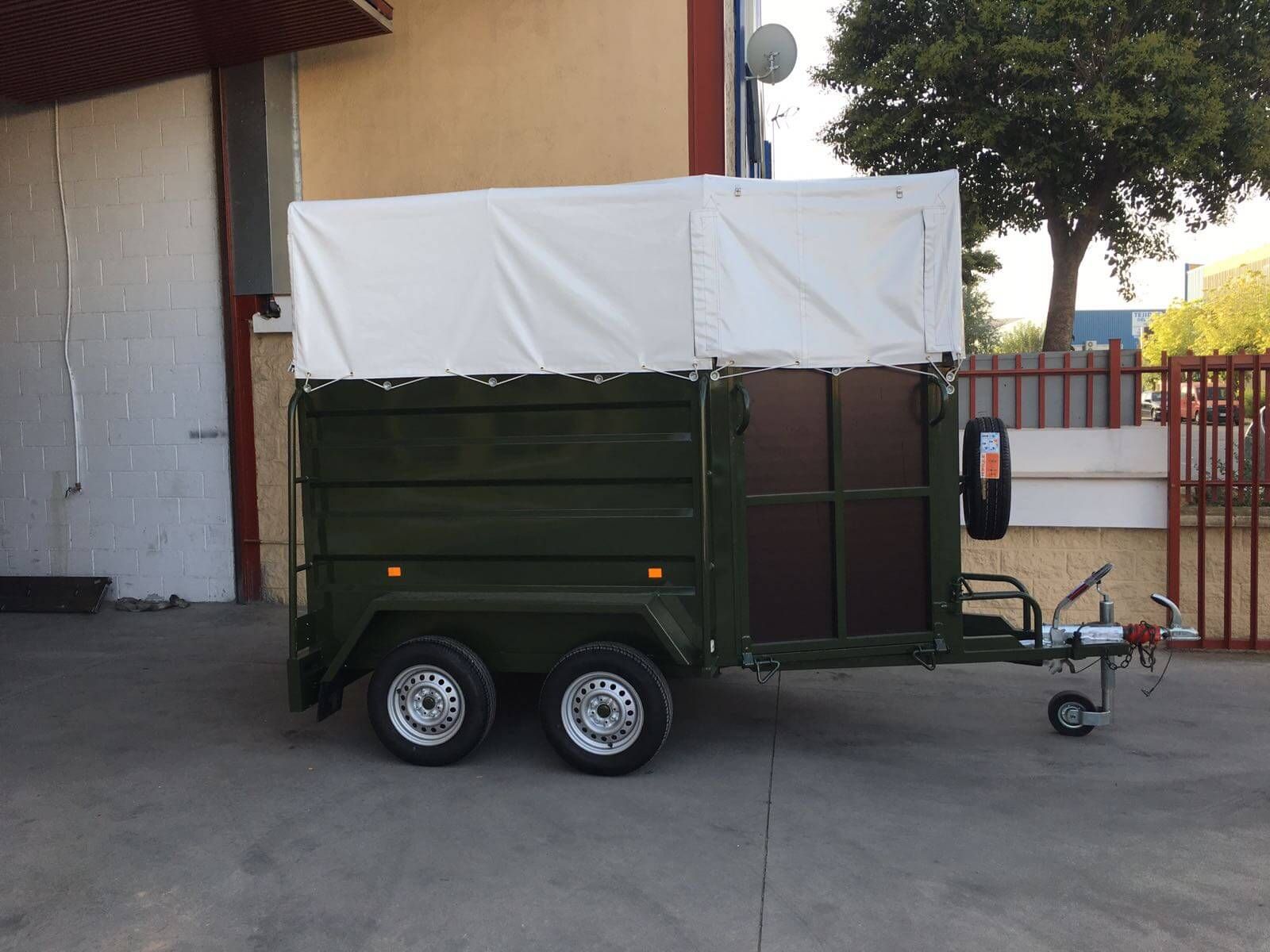 Un remolque verde con una lona blanca encima está estacionado frente a un edificio.