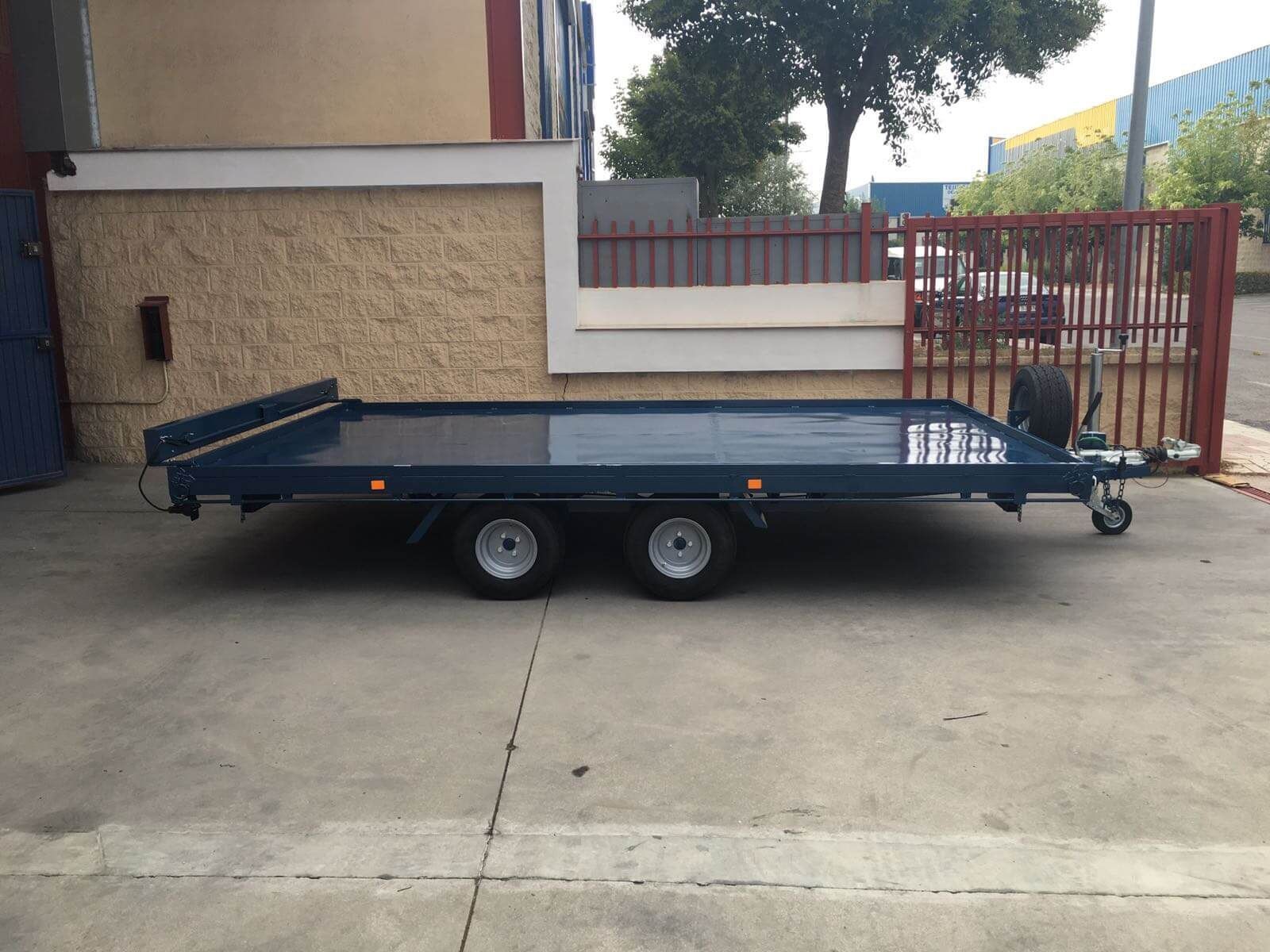 Un remolque de plataforma azul está estacionado frente a un edificio.