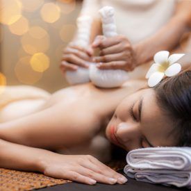 Frau mit einer Blume im Haar erhält in einem Spa eine Kräuterkompressenmassage.