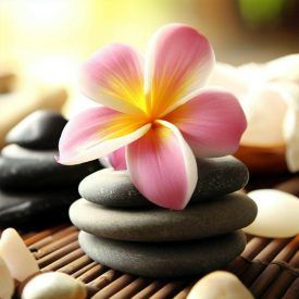 Rosa und gelbe Frangipaniblüten auf einem Stapel grauer Spa-Steine auf einer Bambusmatte.