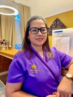 Frau in blauer Uniform sitzt auf goldenem Sofa, davor Blumen, mit Holzwandkunst.