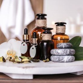 Flaschen mit ätherischen Ölen und Spa-Steinen auf einem weißen Tablett, im Hintergrund ein unscharfes Handtuch.