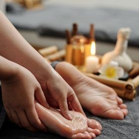 Hände massieren einen Fuß, umgeben von Spa-Behandlungsartikeln wie Öl und Kerzen.