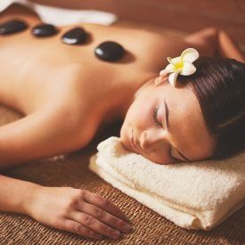 Frau erhält Hot-Stone-Massage im Spa; entspannt mit Blume im Haar.