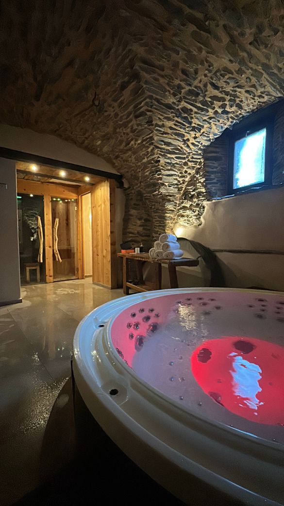 Sala spa con pareti in pietra, vasca idromassaggio rosso acceso e una piccola finestra vicino a una porta di legno.