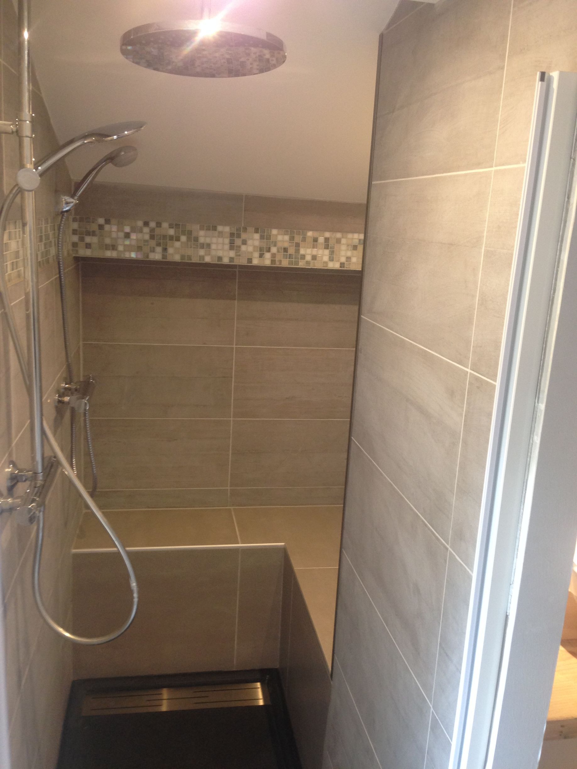 Douche avec carrelage gris, banc, douchette et pommeau de douche effet pluie.