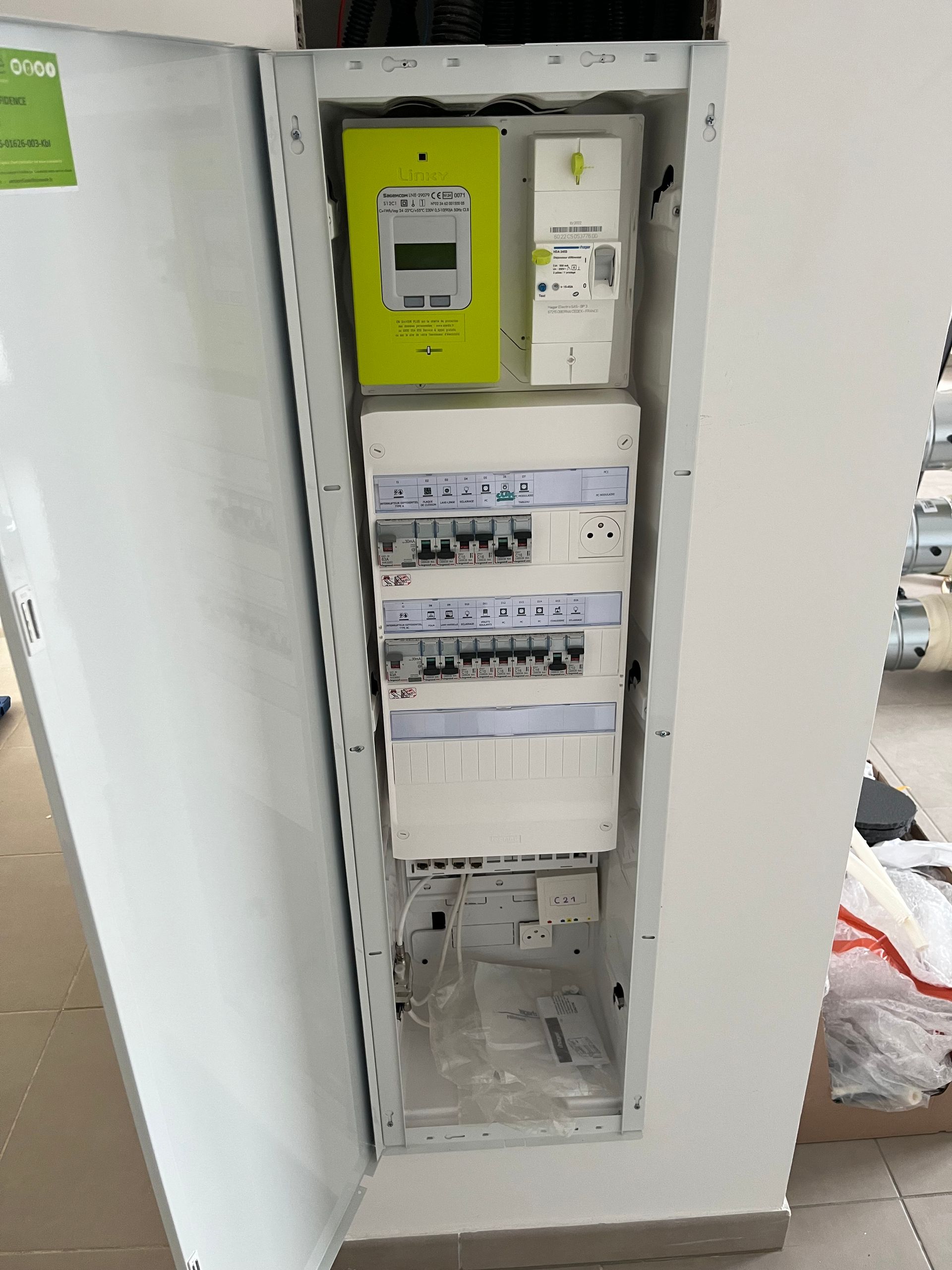 Tableau électrique blanc avec porte ouverte, contenant des compteurs et des disjoncteurs, fixé au mur.