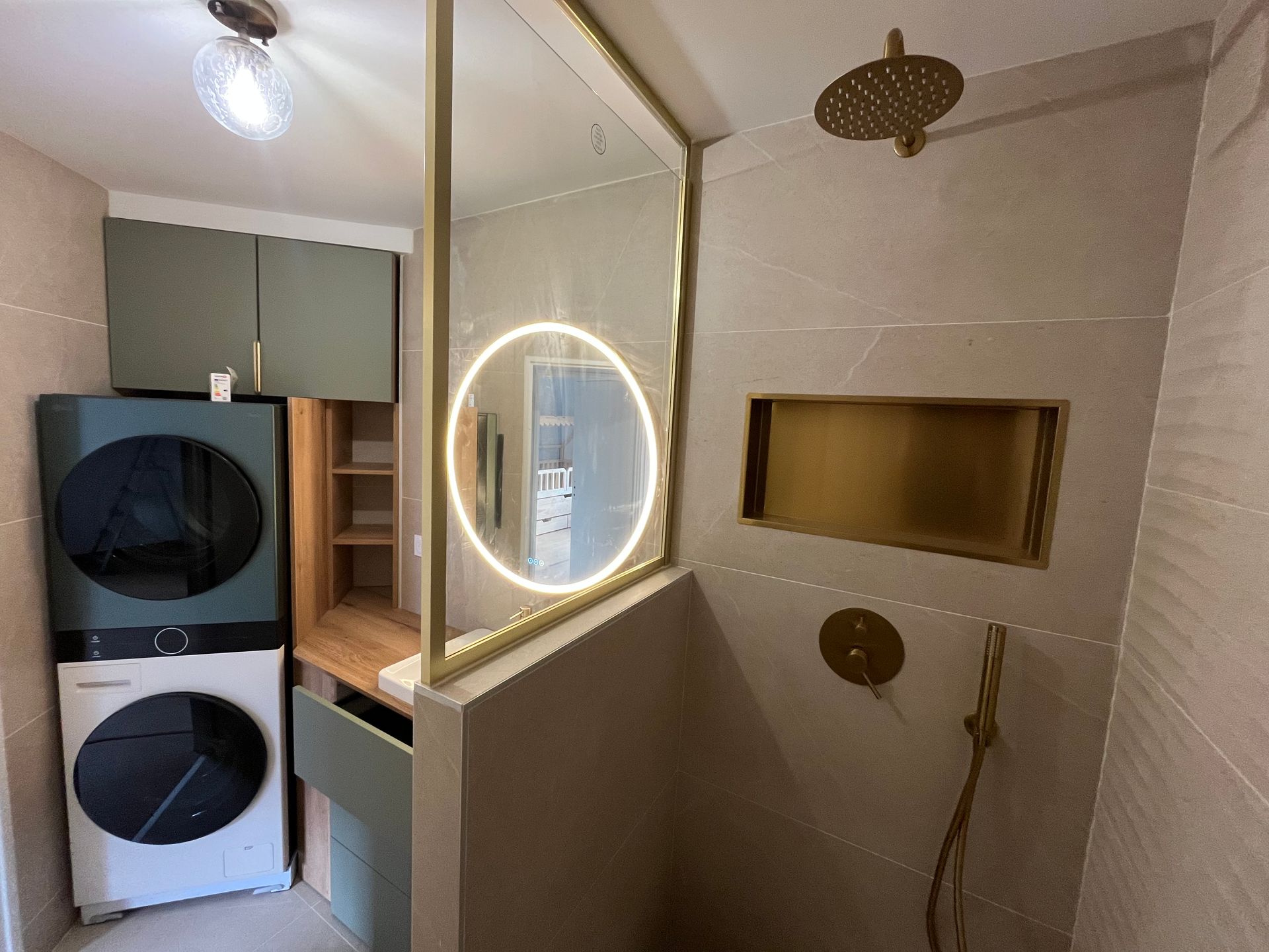 Salle de bains moderne avec robinetterie dorée, douche en verre et laveuse-sécheuse superposées.