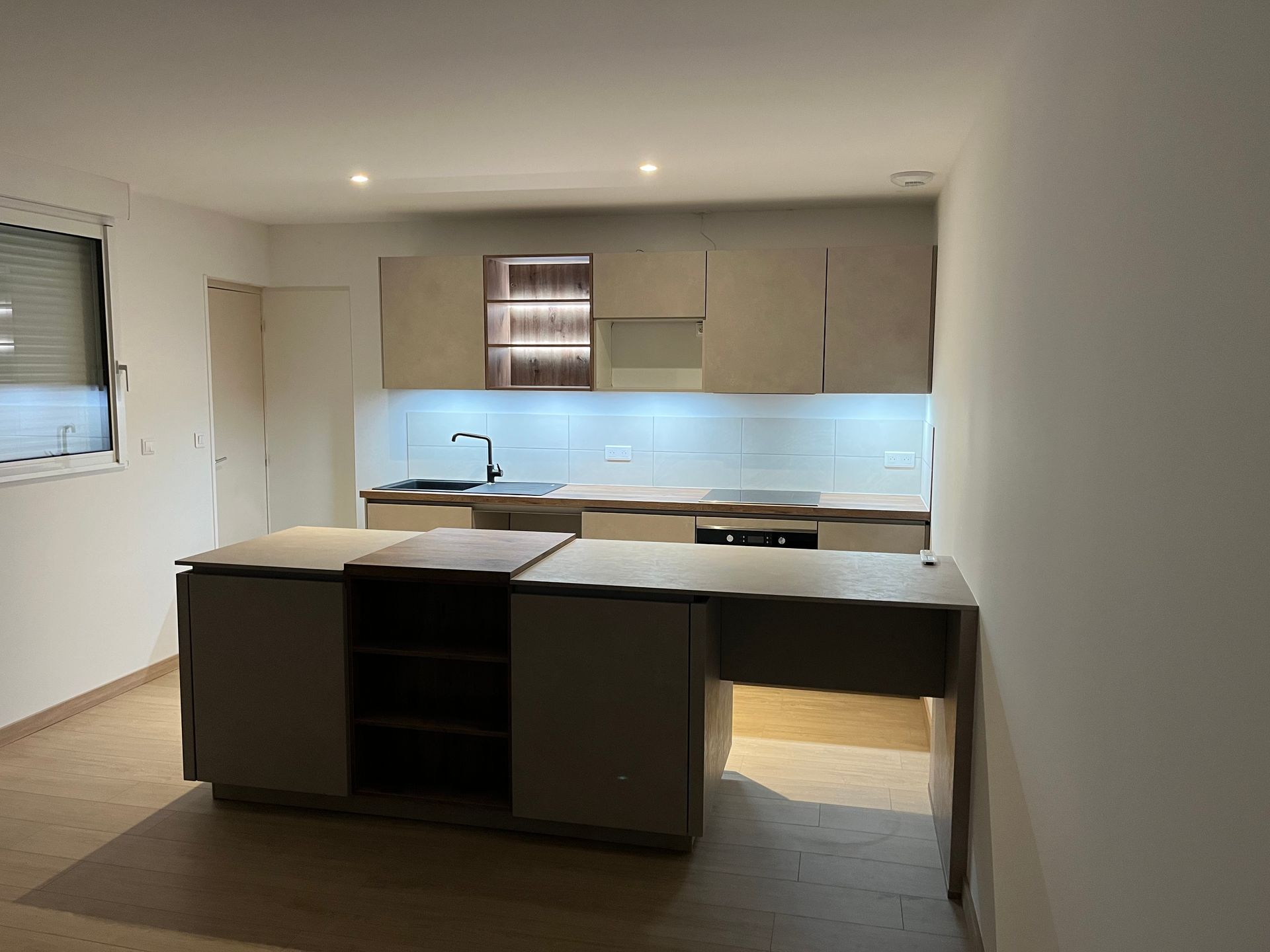 Cuisine moderne avec placards beiges, îlot central et fenêtre.