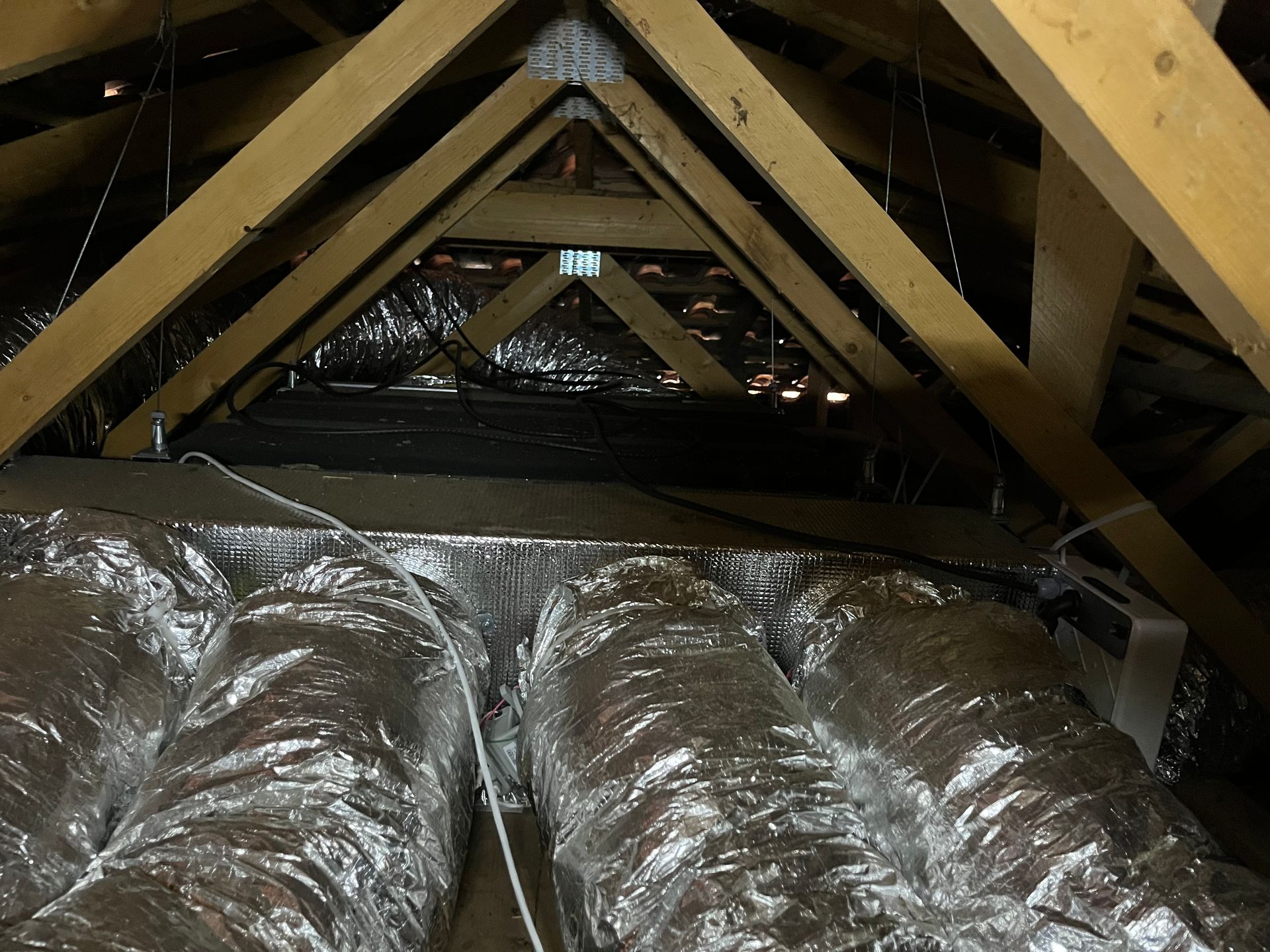 Vue d'un grenier avec des chevrons en bois, des conduits isolés argentés et de la ficelle.